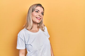 Beautiful caucasian woman wearing casual white t shirt looking away to side with smile on face, natural expression. laughing confident.