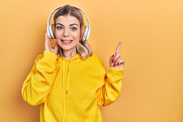 Beautiful caucasian woman listening to music using headphones surprised with an idea or question pointing finger with happy face, number one