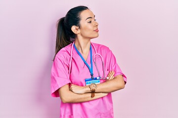 Young brunette woman wearing doctor uniform and stethoscope looking to the side with arms crossed convinced and confident