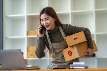 Asian Small business entrepreneur SME working with box and On the phone to confirm orders with customers at home, SME e-commerce digital technology concept.