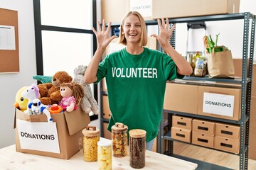 Young caucasian woman wearing volunteer t shirt at donations stand showing and pointing up with...