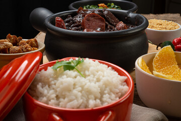 .White rice in the foreground, served in a clay bowl and blurred feijoada in the background