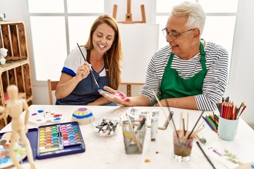 Fototapeta premium Two middle age artists smiling happy painting hands at art studio.
