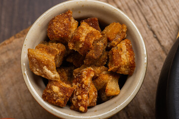 Fried greaves served in a clay bowl on a rustic wooden table