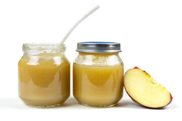 Two glass jars with baby apple puree with a spoon, a gooseberry and an apple slice on a white isolated background. The first fruit lure, baby food.