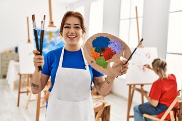 Two artist student women smiling happy painting at art school. Girl holding palette and paintbrushes.