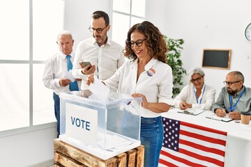 Middle age american voter woman smiling happy putting ballot in voting box at vote center.