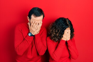 Middle age couple of hispanic woman and man hugging and standing together with sad expression covering face with hands while crying. depression concept.