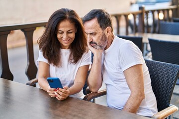 Middle age man and woman couple using smartphone sitting on table at coffee shop terrace