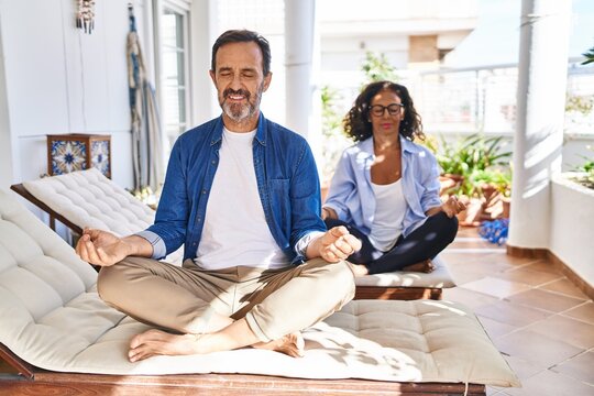Middle age hispanic couple doing yoga exercise sitting on hammock at terrace
