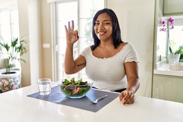 Obraz na płótnie Canvas Young hispanic woman eating healthy salad at home smiling positive doing ok sign with hand and fingers. successful expression.