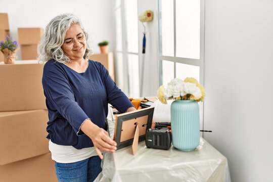 Middle age grey-haired woman smiling happy holding picture at new home.