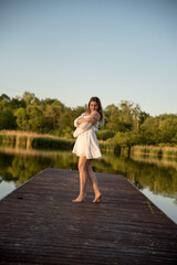 a beautiful girl is standing on the pier. in the background there is a river, a lake.