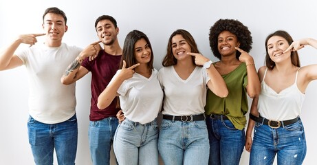 Group of young friends standing together over isolated background smiling cheerful showing and pointing with fingers teeth and mouth. dental health concept.