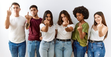 Group of young friends standing together over isolated background showing middle finger, impolite...