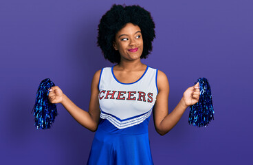 Young african american woman wearing cheerleader uniform using pompom smiling looking to the side...