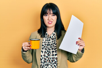 Young hispanic woman wearing business style drinking cup of coffee clueless and confused...