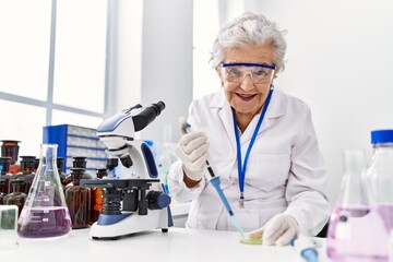 Fototapeta premium Senior grey-haired woman wearing scientist uniform using pipette at laboratory