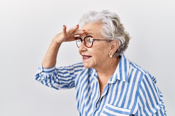 Senior woman with grey hair standing over white background very happy and smiling looking far away with hand over head. searching concept.