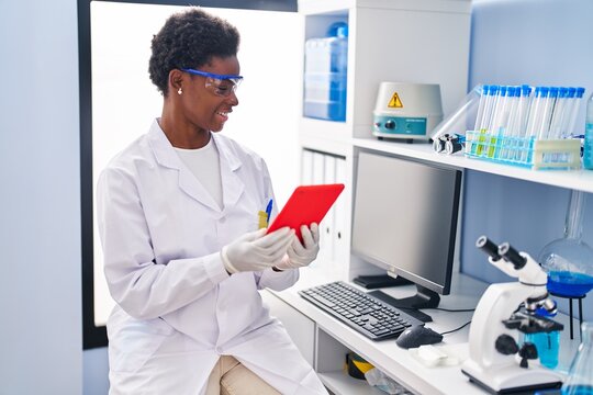 African american woman wearing scientist uniform using touchpad at laboratory