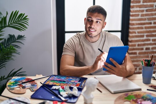 Young hispanic man artist smiling confident using touchpad at art studio