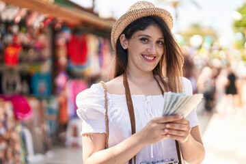 Young hispanic woman tourist smiling confident counting dollars at street market