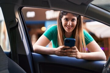 Young hispanic woman using smartphone leaning on window car at street
