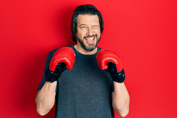 Middle age caucasian man using boxing gloves winking looking at the camera with sexy expression,...