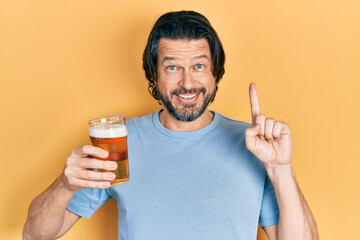 Middle age caucasian man drinking a pint of beer smiling with an idea or question pointing finger...