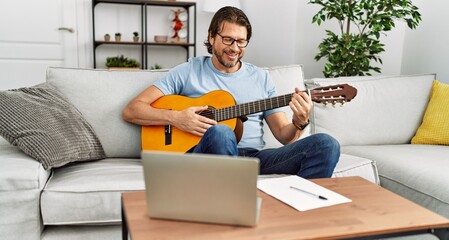 Middle age caucasian man playing classical guitar at home