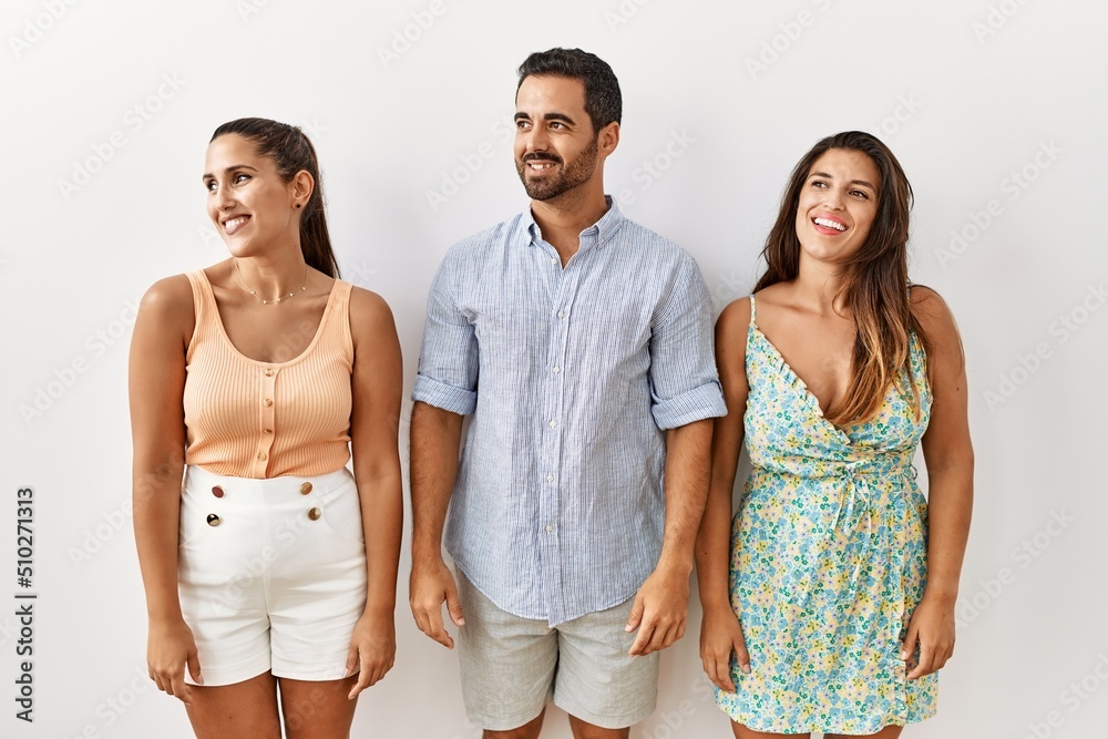 Wall mural Group of young hispanic people standing over isolated background looking away to side with smile on face, natural expression. laughing confident.