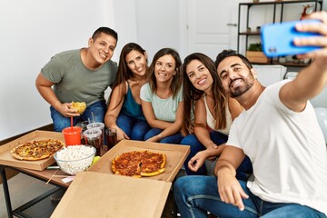 Group of young hispanic friends eating italian pizza make selfie. by the smartphone at home.