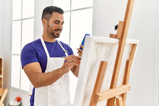 Young hispanic man smiling confident drawing using smartphone at art studio