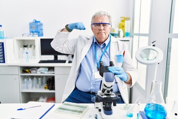 Senior caucasian man working at scientist laboratory strong person showing arm muscle, confident...
