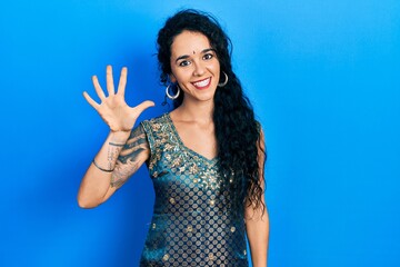 Young woman wearing bindi and traditional kurta dress showing and pointing up with fingers number five while smiling confident and happy.