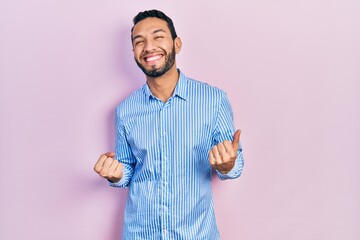 Hispanic man with beard wearing casual blue shirt very happy and excited doing winner gesture with arms raised, smiling and screaming for success. celebration concept.