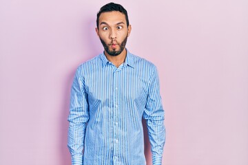 Hispanic man with beard wearing casual blue shirt making fish face with lips, crazy and comical gesture. funny expression.