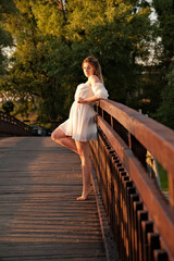 a beautiful girl in a white dress stands on a wooden bridge.