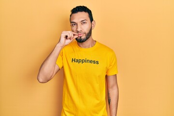 Hispanic man with beard wearing t shirt with happiness word message mouth and lips shut as zip with...