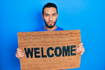 Hispanic man with beard holding welcome doormat relaxed with serious expression on face. simple and natural looking at the camera. © Krakenimages.com