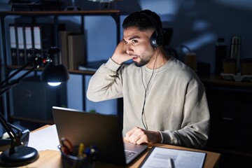 Young handsome man working using computer laptop at night smiling with hand over ear listening an hearing to rumor or gossip. deafness concept.