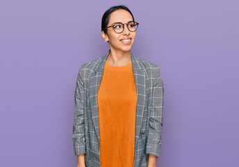 Young hispanic girl wearing business jacket and glasses looking away to side with smile on face, natural expression. laughing confident.