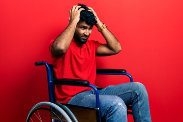 Arab man with beard sitting on wheelchair suffering from headache desperate and stressed because pain and migraine. hands on head.