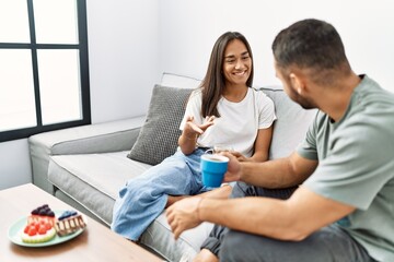 Young latin couple having breakfast sitting on the sofa at home.