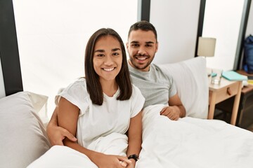 Young latin couple smiling happy hugging on the bed at home.