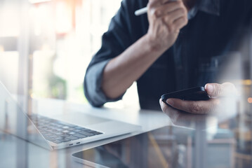 Business man using mobile phone, working on laptop computer, surfing the internet. Man freelancer sitting at table at home office, online working 