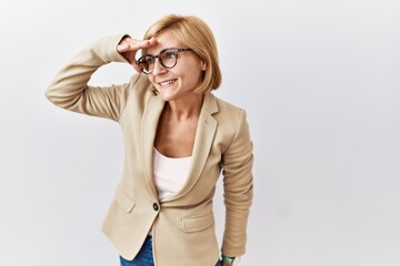 Middle age blonde business woman standing over isolated background very happy and smiling looking far away with hand over head. searching concept.