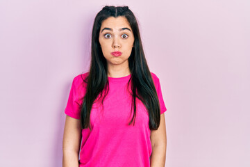 Young hispanic girl wearing casual pink t shirt puffing cheeks with funny face. mouth inflated with...