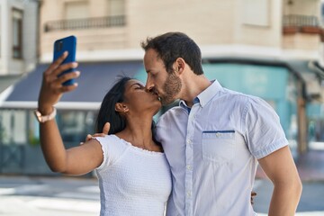 Fototapeta premium Man and woman interracial couple making selfie by smartphone kissing at street
