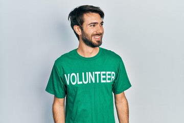 Young hispanic man wearing volunteer t shirt looking away to side with smile on face, natural expression. laughing confident.